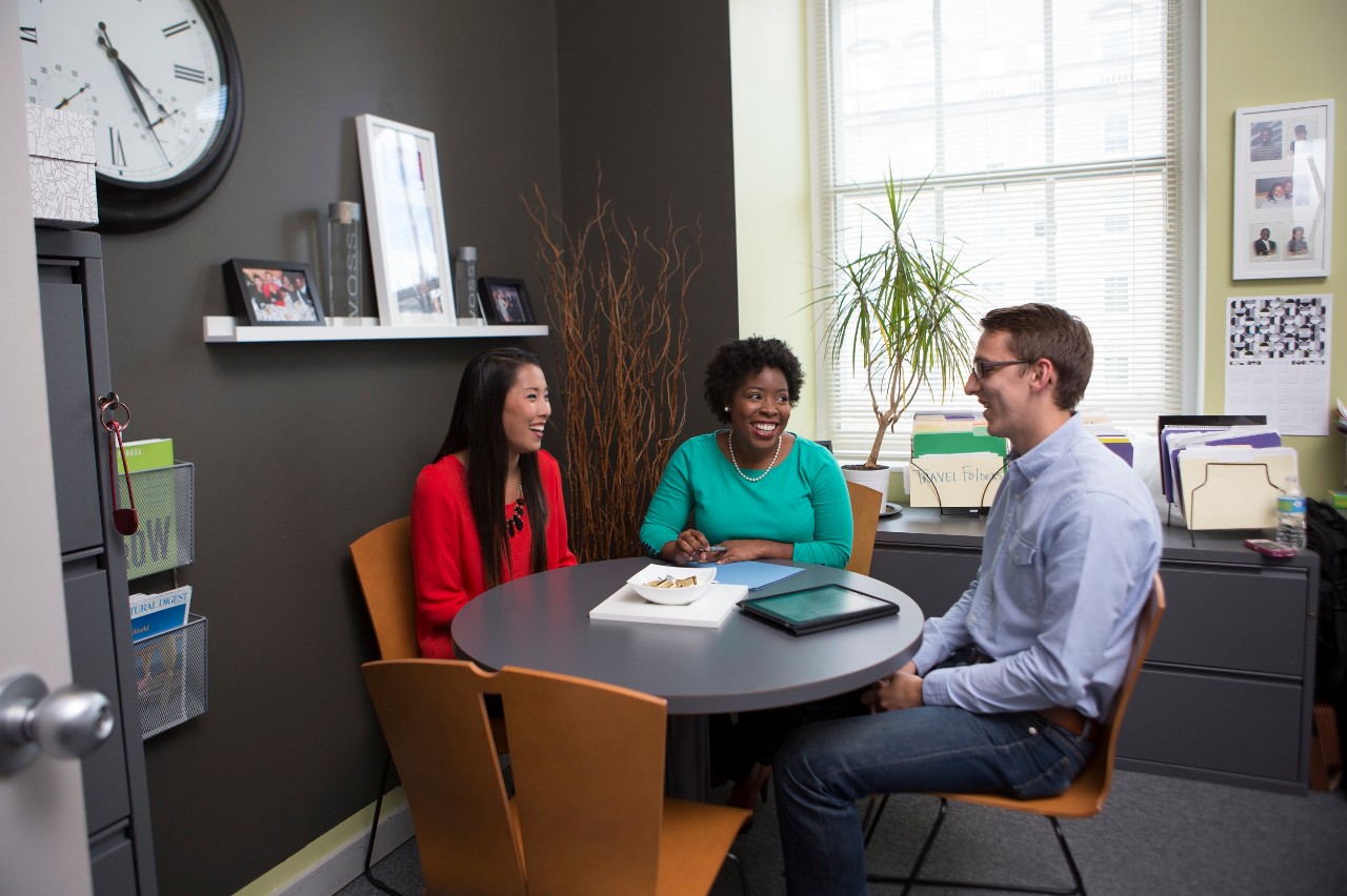 Three people sitting at a round table in an office.